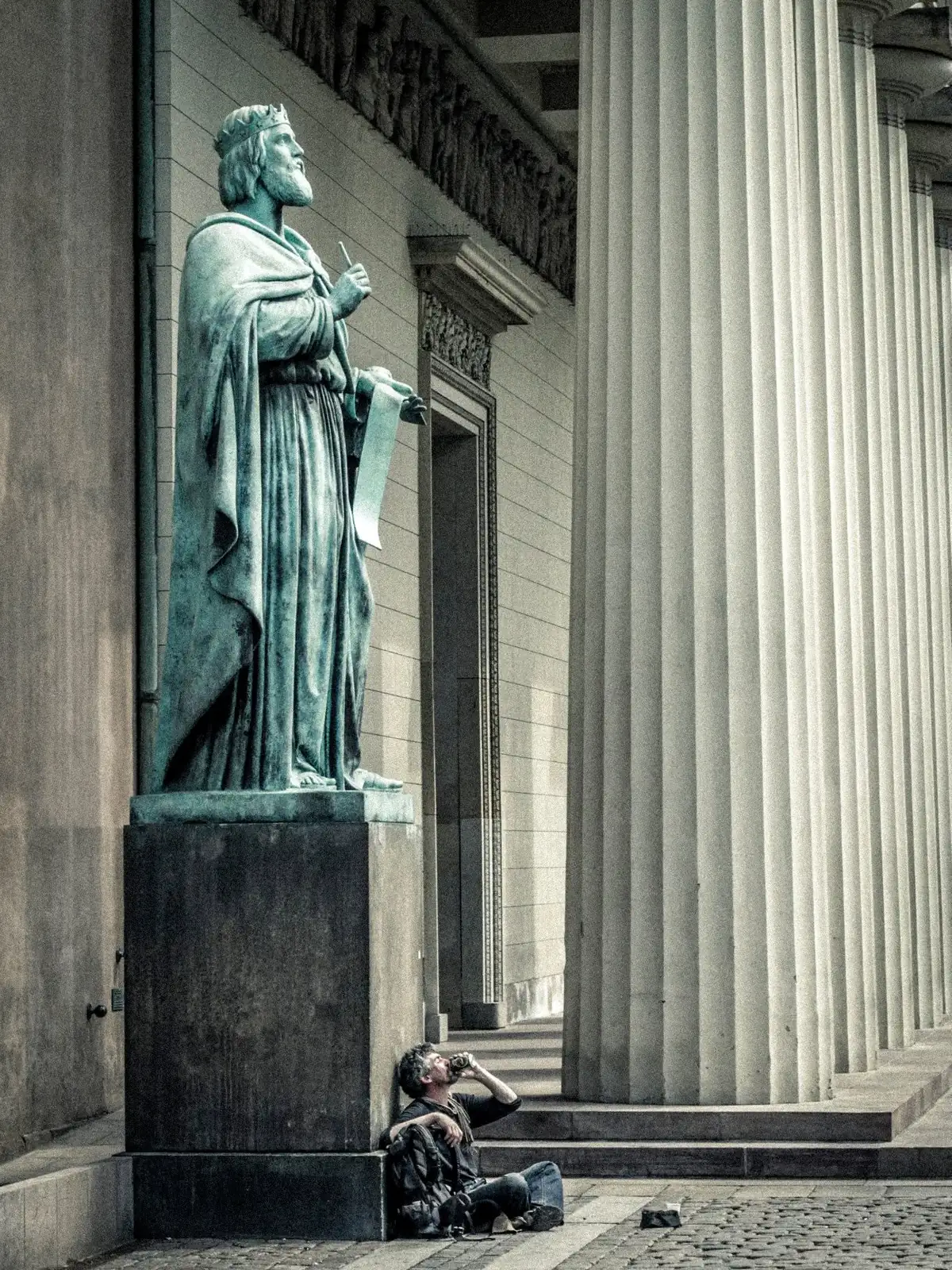A statue and stone columns in Copenhagen, with a person sitting on the steps below.