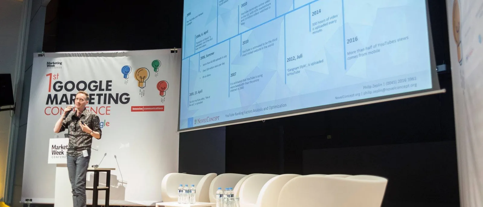Philip Zeplin speaking on stage beside a large presentation screen at a Google Marketing Conference in Athens.